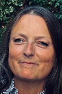 Close-up photograph of a woman with parted hair, smiling and looking slightly left.